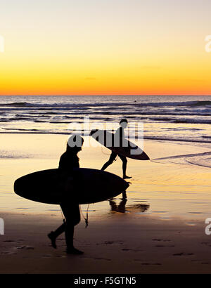 Deux surfer d'exécution sur la plage au coucher du soleil Banque D'Images