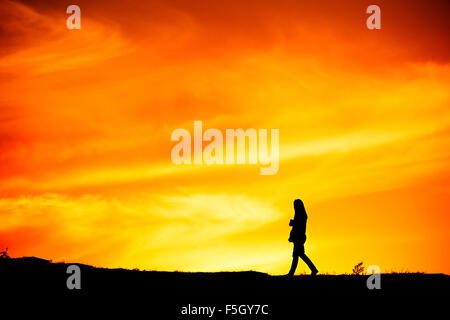 Silhouette d'une femme seule balade au coucher du soleil sur une colline Banque D'Images