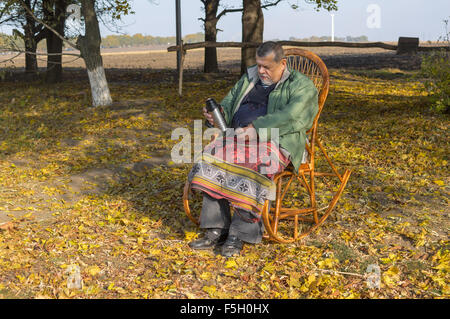 Senior man sitting in wicker chair et prêt à drick plateau à jour d'automne ensoleillé Banque D'Images