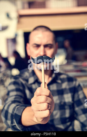 Un young caucasian man holding a fake moustache dans un bâton en face de son visage Banque D'Images