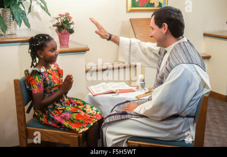 Prêtre catholique bénit fille 7 à 9 ans ans portant plusieurs couleurs robe colorée pendant la synchronisation African American MR ©Myrleen Pearson....Ferguson Cate Banque D'Images