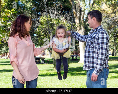 Père, mère et jeune fille jouer sur les balançoires du parc Banque D'Images