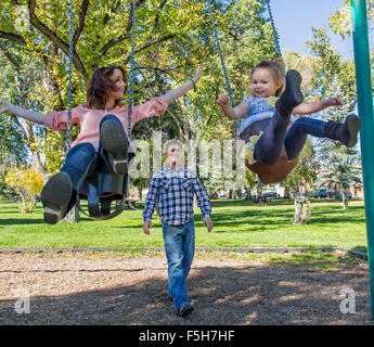 Père, mère et jeune fille jouer sur les balançoires du parc Banque D'Images