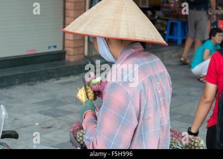 Dame vietnamienne se tenait à Hanoi old quarter en utilisant le couteau à peler et couper l'ananas frais, Vietnam Banque D'Images