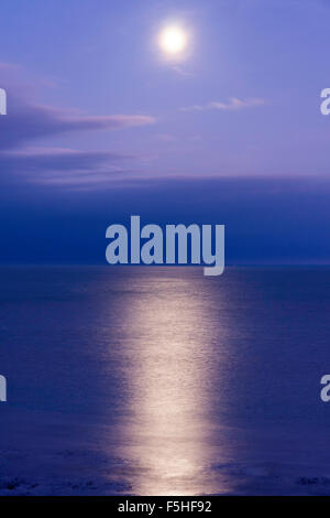 Super pleine Lune brillant dans un ciel bleu mauve sur une mer de palourdes, la Manche, au large de la côte du Kent à Ramsgate, avec grande réflexion. Quelques nuages. Banque D'Images