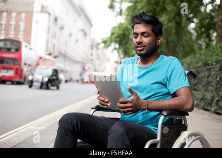 Homme handicapé dans un fauteuil roulant à l'aide d'un ordinateur tablette dans la rue Banque D'Images