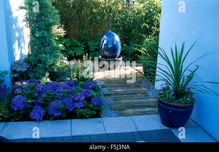 Hortensia bleu en été lit à côté d'un patio avec une fontaine en céramique bleu et phormium dans un pot bleu Banque D'Images