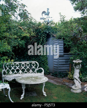 Fer forgé blanc Banc et table de jardin avec une statue en pierre et un petit hangar bleu Banque D'Images