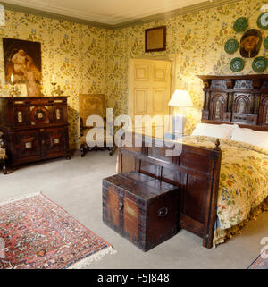 Coffre en chêne antique en bois sculpté au-dessous de lit de style jacobéen dans un pays chambre avec revêtement mural en tissu Banque D'Images