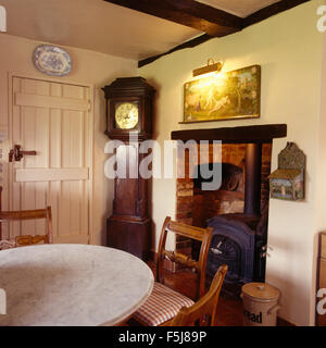 Horloge antique en coin d'une maison traditionnelle des années 80 salle à manger avec un poêle à bois dans une petite cheminée Banque D'Images