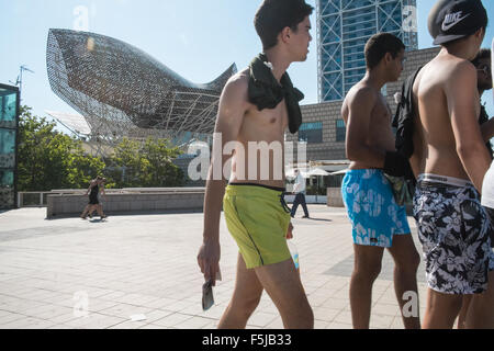 Les gars en shorts passant de Frank Gehry Peix sculpture de poisson à la plage de Barceloneta,urbain,plage de Barcelone Catalogne, Espagne. Banque D'Images