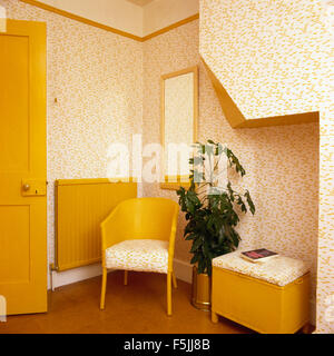 Chaise Lloyd Loom peint jaune et panier à linge dans une salle de bains avec papier peint fleuri 70 Banque D'Images