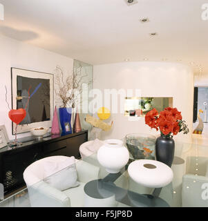 Vases en céramique blanche et d'un vase de l'amaryllis rouge sur une table en verre avec chaises blanches dans une salle à manger des années 90 Banque D'Images