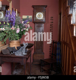 Arrangement de fleurs d'été sur table console dans un hall cottage rose des années 90 avec une horloge antique et chaise en bois Banque D'Images