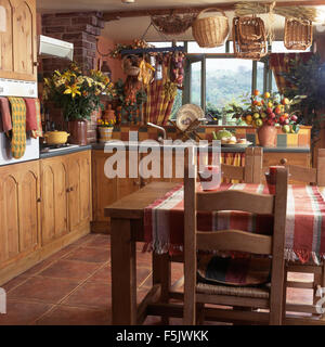 Chaises en bois rustique à table avec un chiffon contrôlée dans un pays cuisine avec portes en pin sur des unités montées et paniers au plafond Banque D'Images