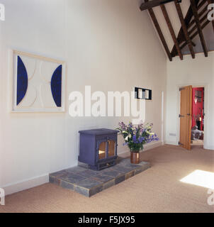 Vase de fleurs d'ardoise bleue sur socle avec poêle à bois dans la grange aménagée moderne salle avec tapis en sisal beige Banque D'Images
