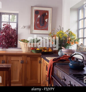 Panier de légumes et de vase de fleurs colorées sur plan en blanc chalet cuisine avec plaque de cuisson théière sur bleu Banque D'Images