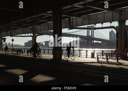 Deux hommes et un autre cycle de promenades le long de l'East River Esplanade, à New York, sous le viaduc de la rivière East Roosevelt Banque D'Images