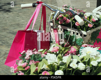 Décorées avec un vélo rose sacoches pleines de fleurs et un panier sur le guidon garé dans une rue pavée Banque D'Images