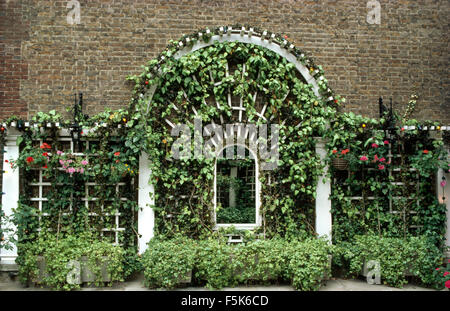 Des puce dans les treillis verts avec des semoirs ci-dessous les plantes sur une fenêtre en arc Banque D'Images