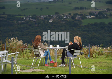 2 femmes amies assises à l'extérieur, mangeant et discutant au café Cow & Calf Rock, Ilkley, Yorkshire, Royaume-Uni - endroit pittoresque avec vue panoramique sur la vallée. Banque D'Images