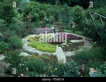 De plus en plus d'herbes dans un lit circulaire bordé d'un chemin pavé en pierre dans un grand pays jardin en été Banque D'Images