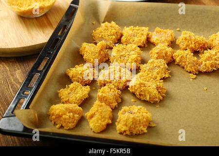 Panés fraîchement dans les flocons de maïs filet de poulet sur une plaque à pâtisserie. Faire cuite au four miettes de flocons de maïs nuggets de poulet. Série. Banque D'Images