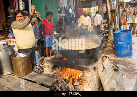 Dans le marché de Varanasi un homme est en train de préparer un délicieux repas indien dans une cocotte sur un feu de bois Banque D'Images