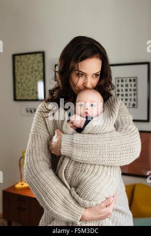 Woman kissing baby son, l'enveloppant dans son cardigan Banque D'Images