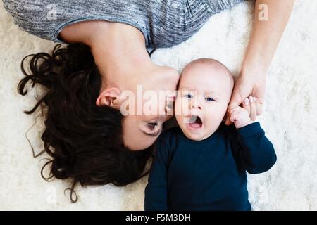 Mère couchée sur un tapis et embrassant bébé fils sur joue, overhead view Banque D'Images