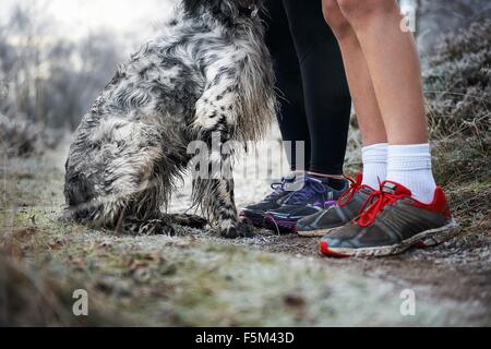 Les jambes de la mère et le fils portant des formateurs et chien assis Banque D'Images