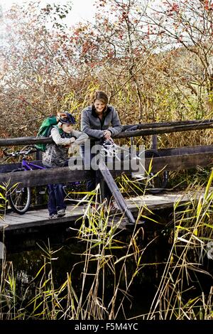 Mère et fils avec des vélos debout sur la passerelle en bois à la rivière au bas Banque D'Images