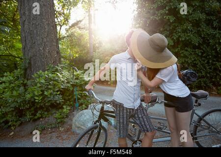 Jeune couple avec cycle tandem kissing on rural road Banque D'Images