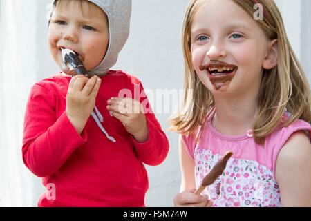 Female toddler et salissent soeur manger du chocolat glaces Banque D'Images