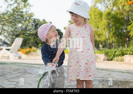 Fille et tout-petit sœur jouant avec de l'eau arrosage de jardin Banque D'Images