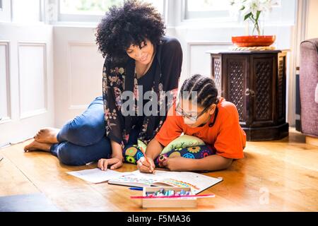 Femme mature et fils faisant sketchbook devoirs sur plancher du salon Banque D'Images
