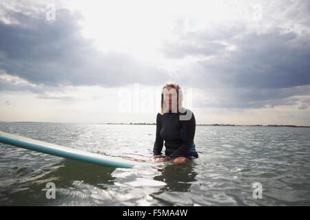 Portrait of senior woman sitting on surfboard in sea Banque D'Images