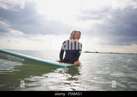 Senior woman sitting on surfboard in sea Banque D'Images