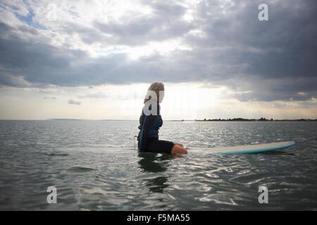 Senior woman sitting on surfboard en mer, vue arrière Banque D'Images