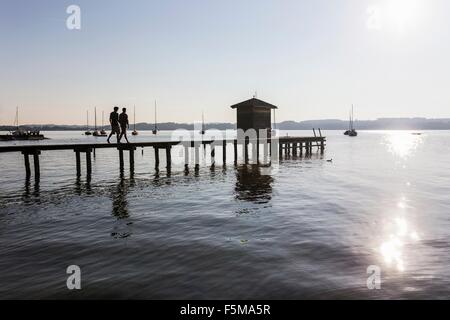 Silhouette de couple en train de marcher sur la jetée au lac d'un hangar à bateaux, Schondorf am Ammersee,, Bavière, Allemagne Banque D'Images