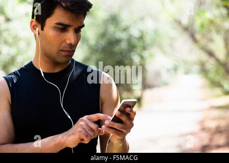 Jogger sélection de musique sur smartphone in park Banque D'Images