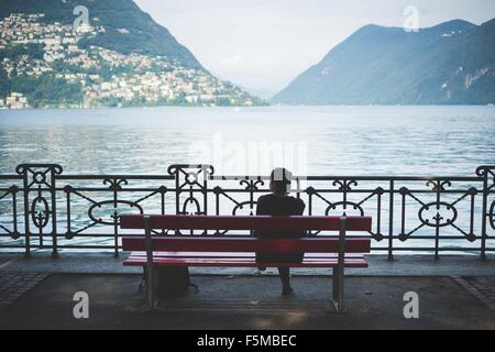 Vue arrière de la silhouette femme sur banc de parc avec vue sur le lac de Lugano, Suisse Banque D'Images