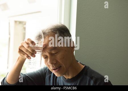 Mature man holding bouteille d'eau pour le front les yeux fermés Banque D'Images