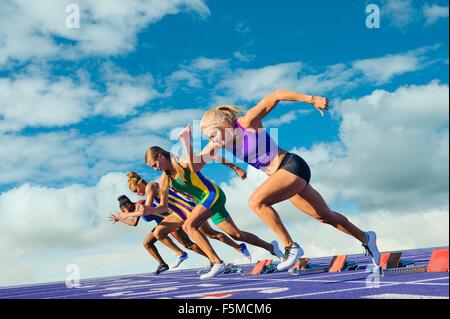 Quatre femmes athlètes sur piste d'athlétisme, laissant starting-blocks Banque D'Images