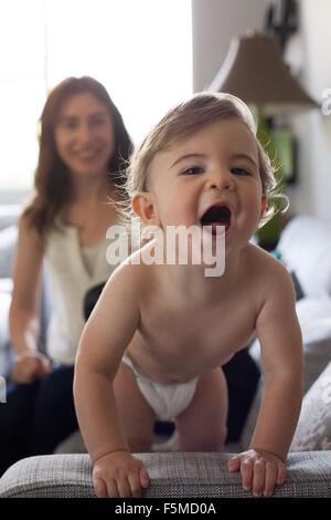 Baby Boy holding sur canapé à la bouche ouverte de l'appareil photo à Banque D'Images