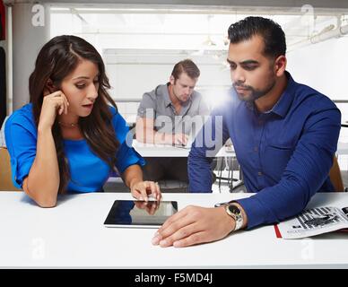 Young businessman sitting at desk, looking at digital tablet Banque D'Images