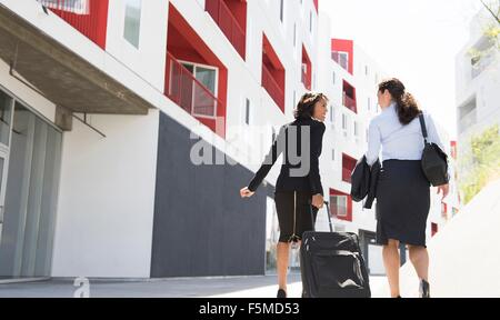 Two businesswomen walking along street, suitcase, vue arrière Banque D'Images