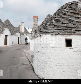 Un vieil homme marche dans une rue entourée par les trulli d'Alberobello, Province de Bari, Puglia, Italie Banque D'Images