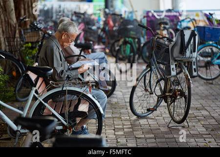 Vieux chinois lire le journal par Cheung Chau Port, entouré de banlieue en Stationnement des vélos. Hong Kong. Banque D'Images