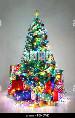 Arbre de Noël décoré avec des lumières colorées entouré par des cadeaux. Banque D'Images